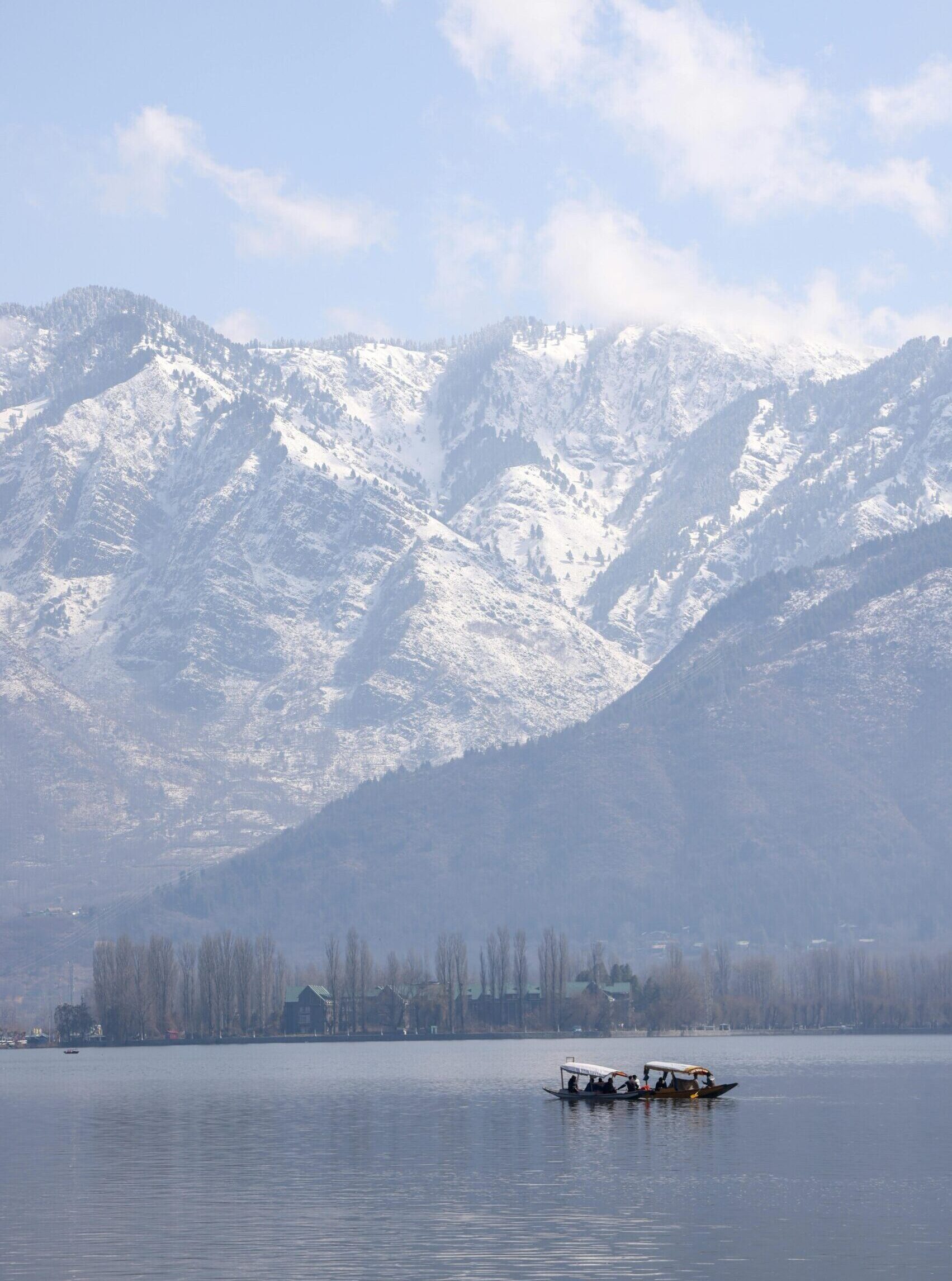 Traditional boats carrying tourists on a serene lake with snow-capped mountains