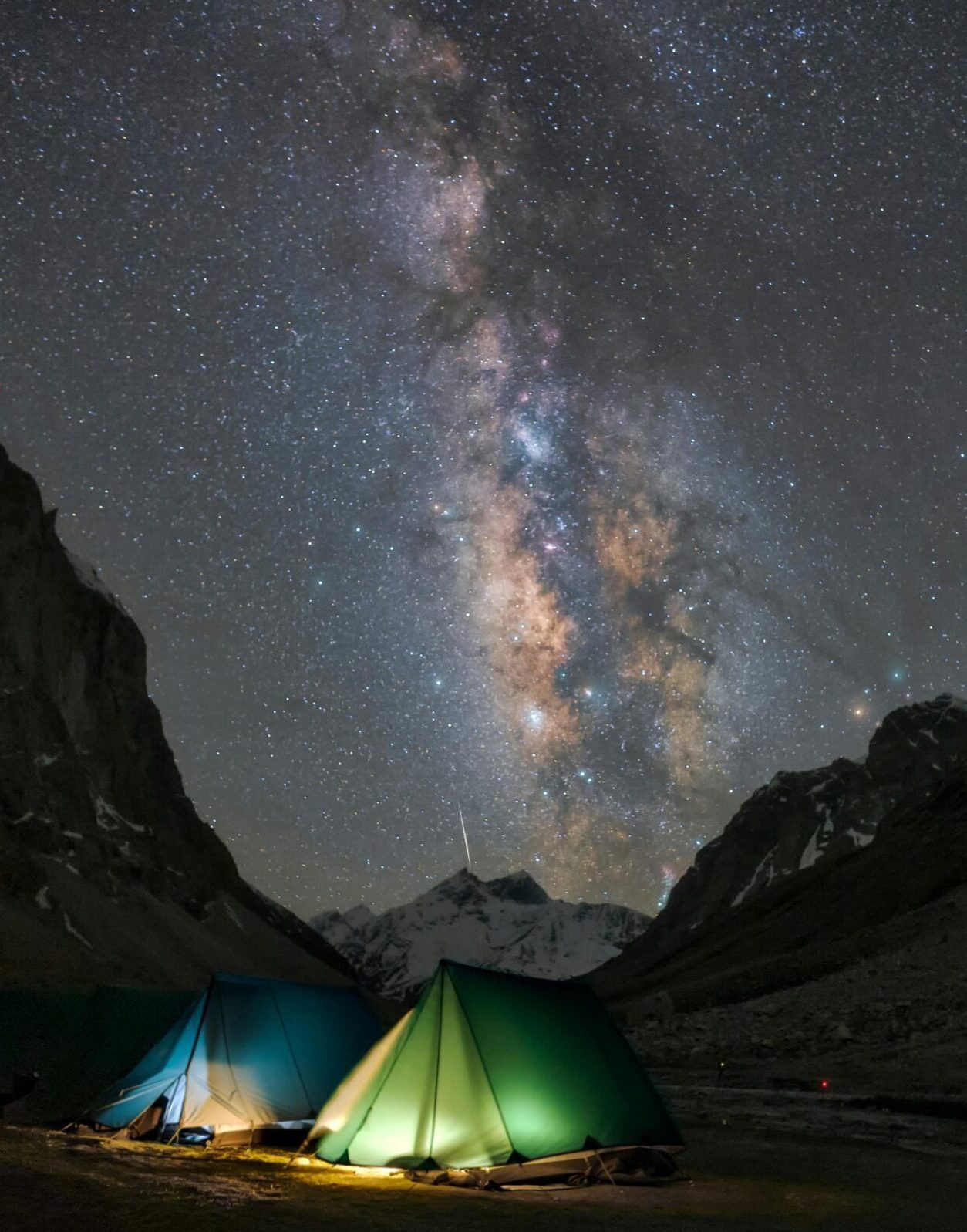 Camping tents under the Milky Way in a mountain valley with star-filled skies.