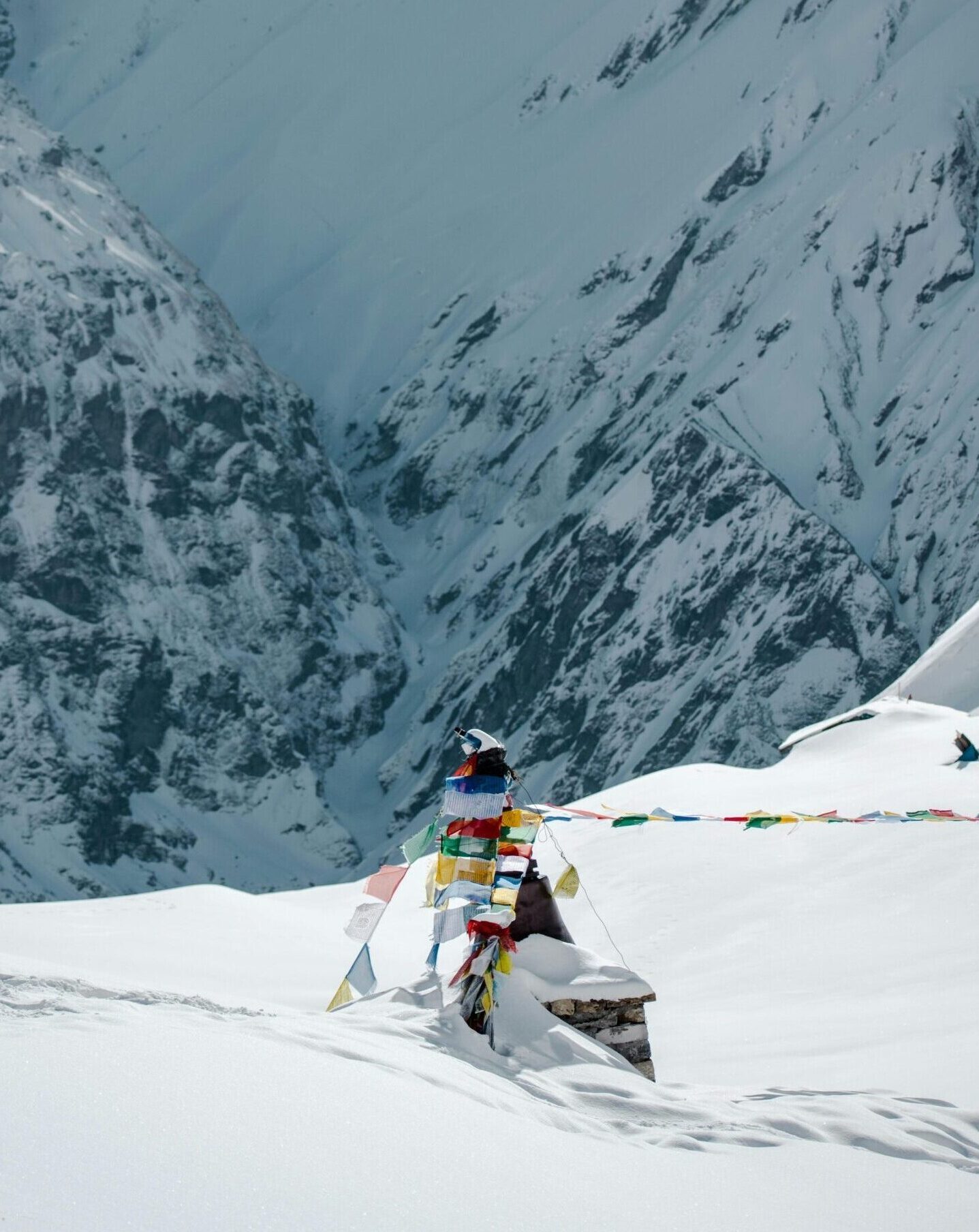 Colorful Tibetan prayer flags in snow with steep Himalayan peaks in the background.